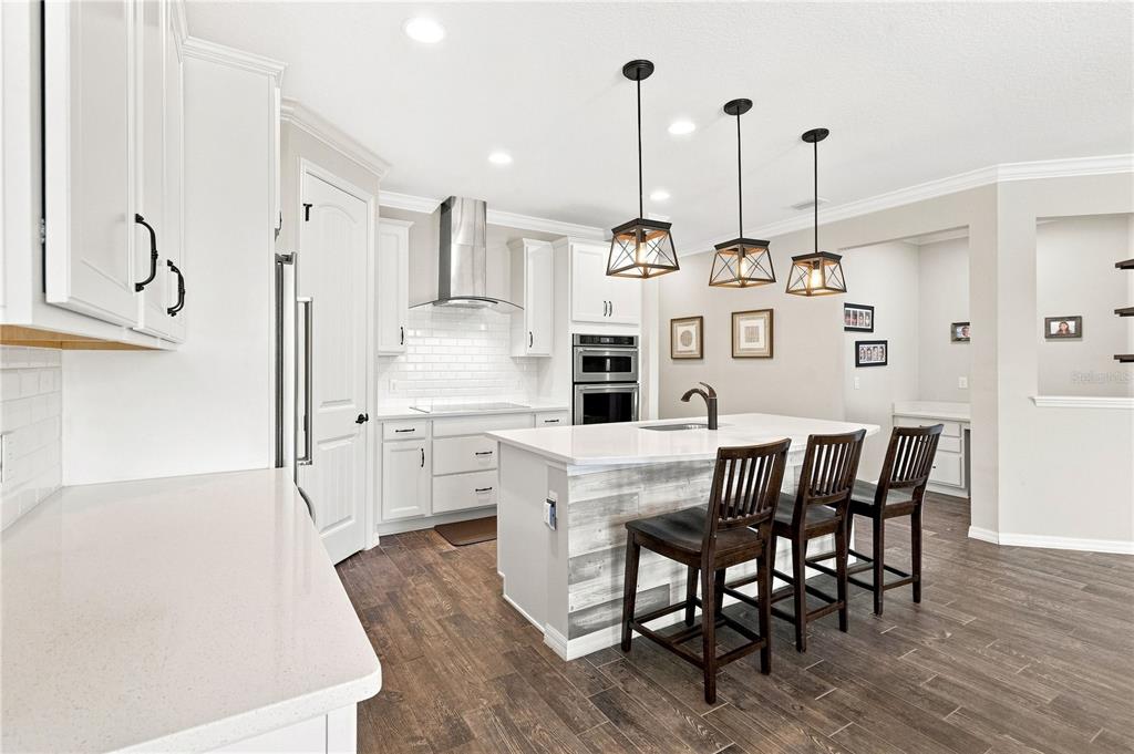 A modern kitchen features white cabinets, a central island with bar seating, and wood-look flooring — 7278 TWILIGHT BAY DRIVE, WINTER GARDEN, FL