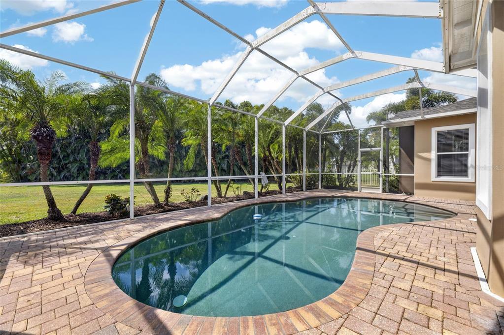 A screened-in patio features a kidney-shaped swimming pool surrounded by brick pavers and palm trees — 824 ISLEBAY DRIVE, APOLLO BEACH, FL