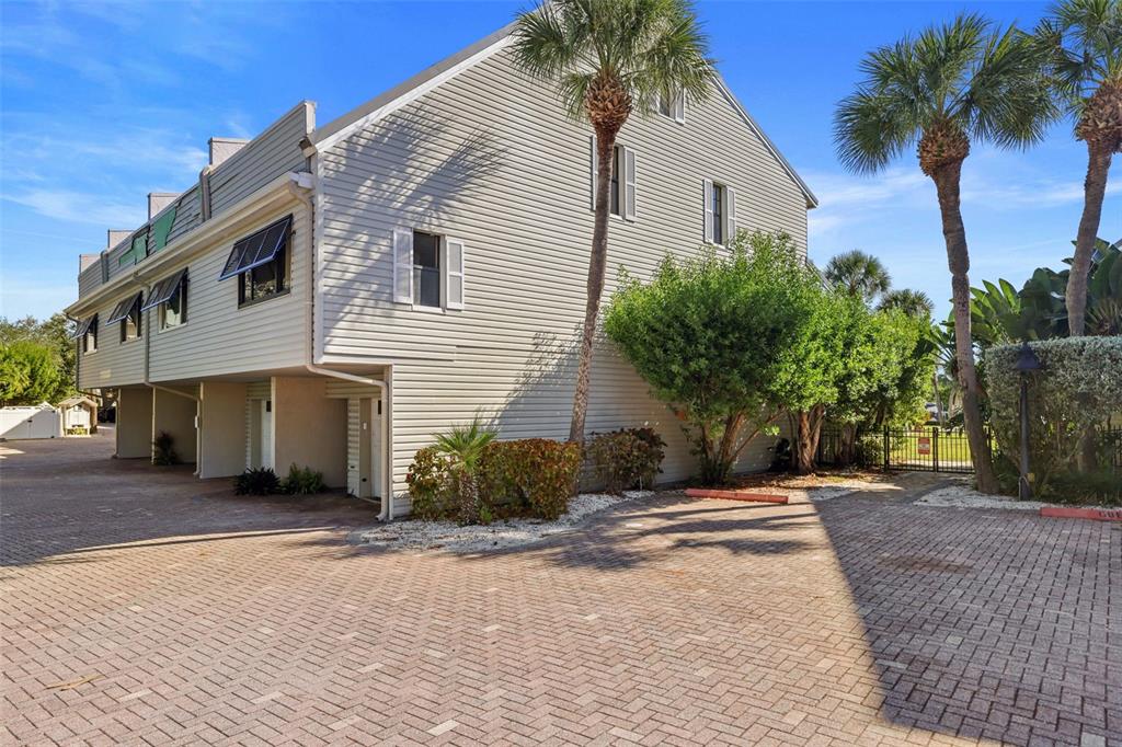 A multi-story townhouse with light siding, a brick driveway, and palm trees on a sunny day — 1355 PINELLAS BAYWAY S UNIT 19, TIERRA VERDE, FL