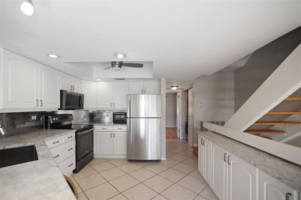 A kitchen with white cabinets, stainless steel appliances, marble-look countertops, and tile flooring — 1355 PINELLAS BAYWAY S UNIT 19, TIERRA VERDE, FL