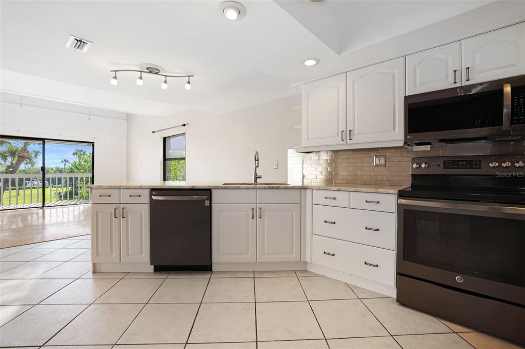 A kitchen with white cabinets, dark appliances, and tile flooring opens to a balcony view — 1355 PINELLAS BAYWAY S UNIT 19, TIERRA VERDE, FL