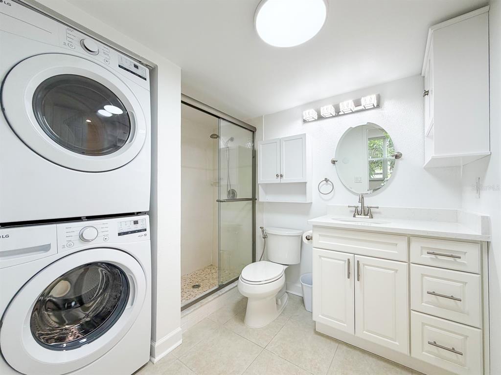 A bathroom features a stacked washer and dryer, a glass-enclosed shower, and a white vanity — 7625 SUN ISLAND DRIVE S UNIT 101, SOUTH PASADENA, FL