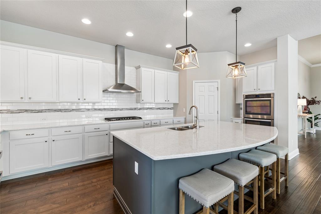 A kitchen features white cabinetry, a blue island with four stools, and stainless steel appliances — 7223 HOURGLASS DRIVE, APOLLO BEACH, FL