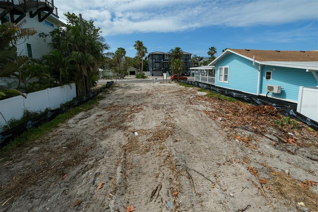 A vacant, sandy residential lot is enclosed by black silt fencing with two real estate signs — 106 S 11TH, BRADENTON BEACH, FL