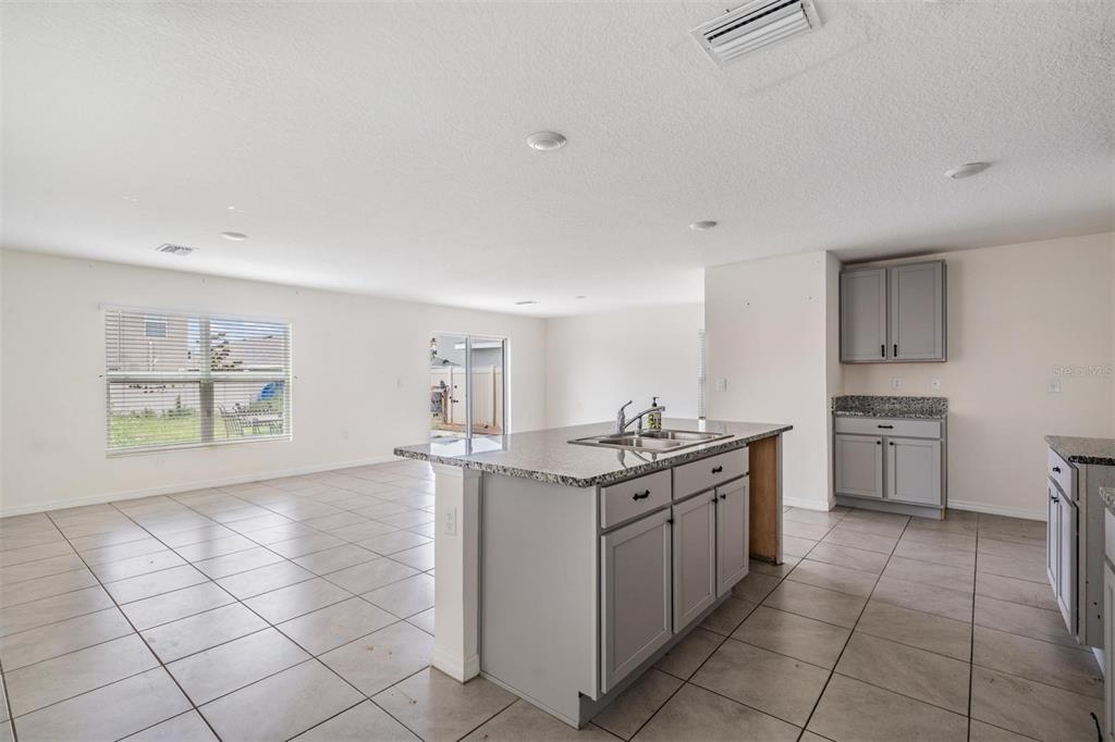 A kitchen with a granite-topped island and gray cabinets opens into a tiled living area — 12175 WATER ASH PLACE, RIVERVIEW, FL