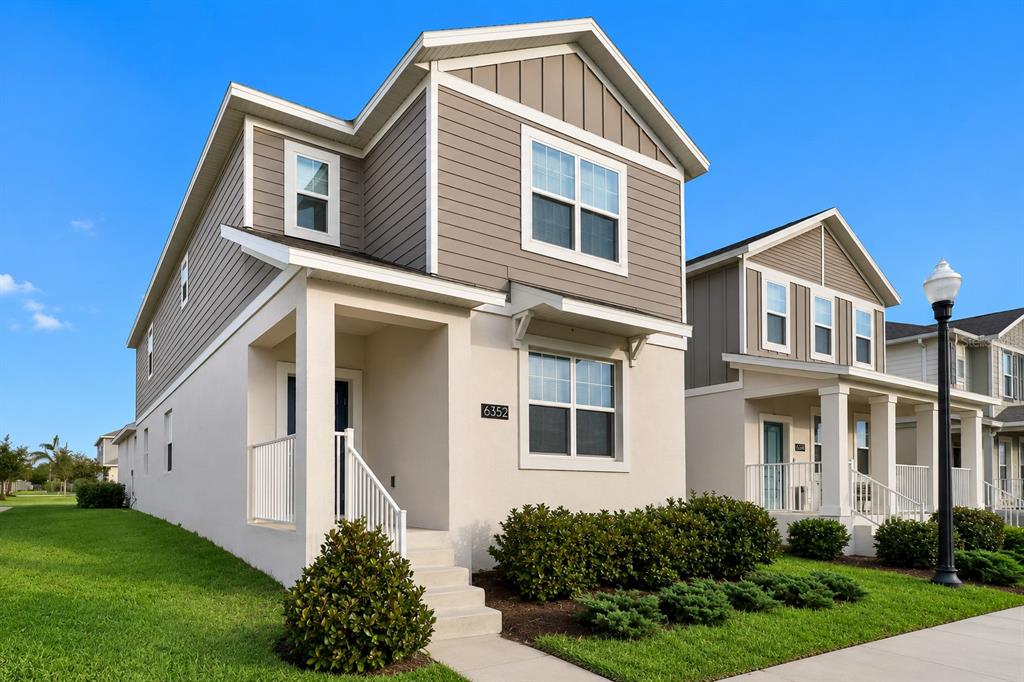 A two-story house with beige stucco, gray siding, and a front porch under a blue sky — 6352 SPRUCEPINE LANE, ST CLOUD, FL