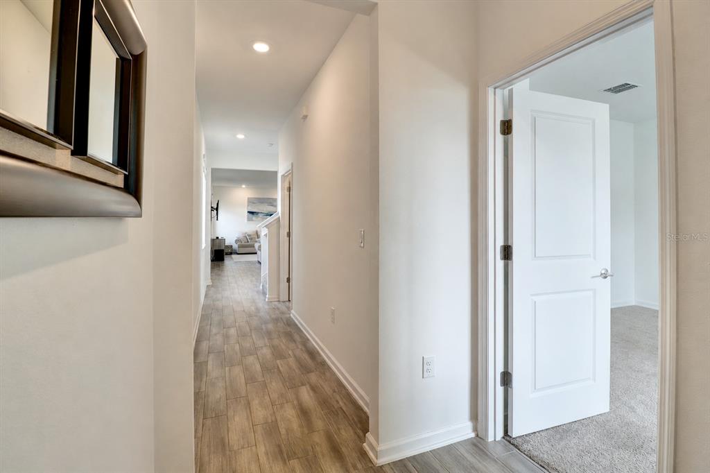 A hallway with wood-look tile flooring leads to a room with carpeted floors — 6352 SPRUCEPINE LANE, ST CLOUD, FL