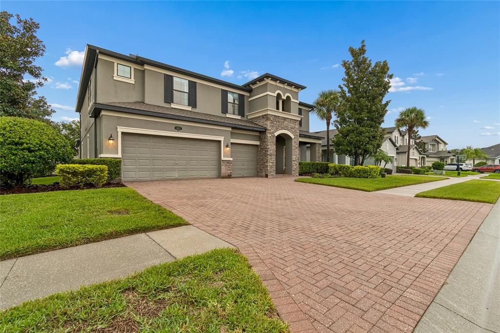 A two-story suburban house with a brick paver driveway and a three-car garage — 1657 FEATHER GRASS LOOP, LUTZ, FL