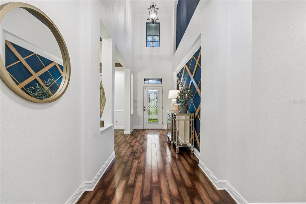 A bright entryway features high ceilings, dark wood flooring, and blue accent walls with lattice — 1657 FEATHER GRASS LOOP, LUTZ, FL
