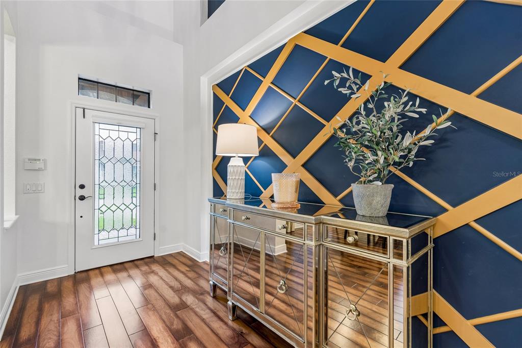 An entryway features a mirrored console table against a blue wall with gold geometric trim — 1657 FEATHER GRASS LOOP, LUTZ, FL