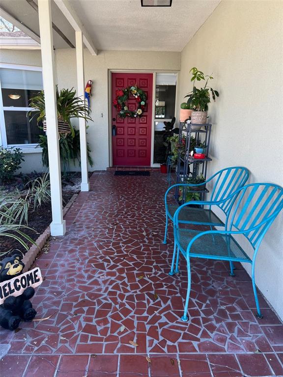 A covered front porch features a red door, mosaic tile flooring, and two turquoise chairs — 855 FOUNTAINHEAD DRIVE, LARGO, FL
