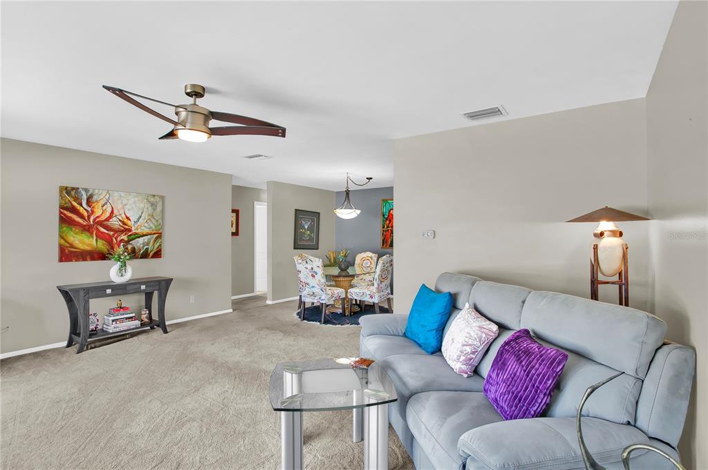 A living room with gray carpet, a light blue sofa, and a dining area beyond — 855 FOUNTAINHEAD DRIVE, LARGO, FL