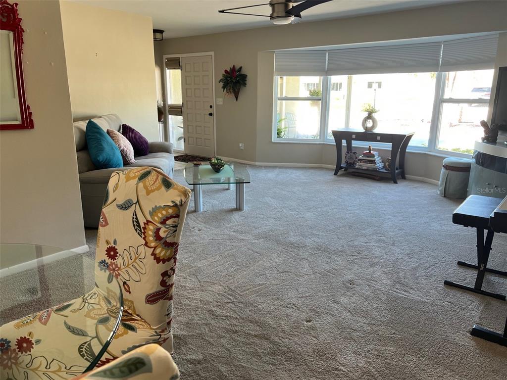 A living room with beige carpet, a glass coffee table, and a large bay window — 855 FOUNTAINHEAD DRIVE, LARGO, FL