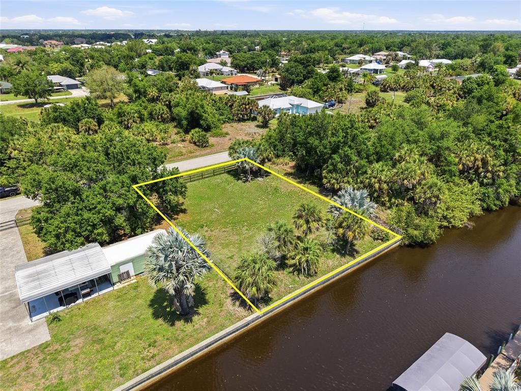 An aerial view shows a vacant, fenced waterfront lot with palm trees next to a house — 28451 SABAL PALM DRIVE, PUNTA GORDA, FL