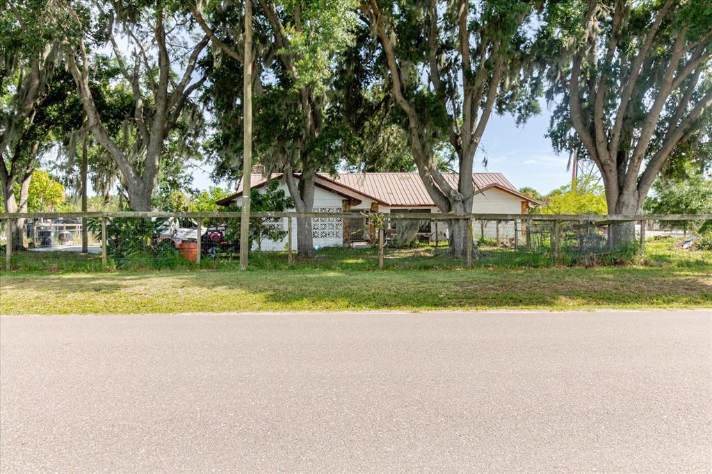 A single-story house with a metal roof sits behind a wooden fence and large trees — 11109 SUMNER ROAD, WIMAUMA, FL