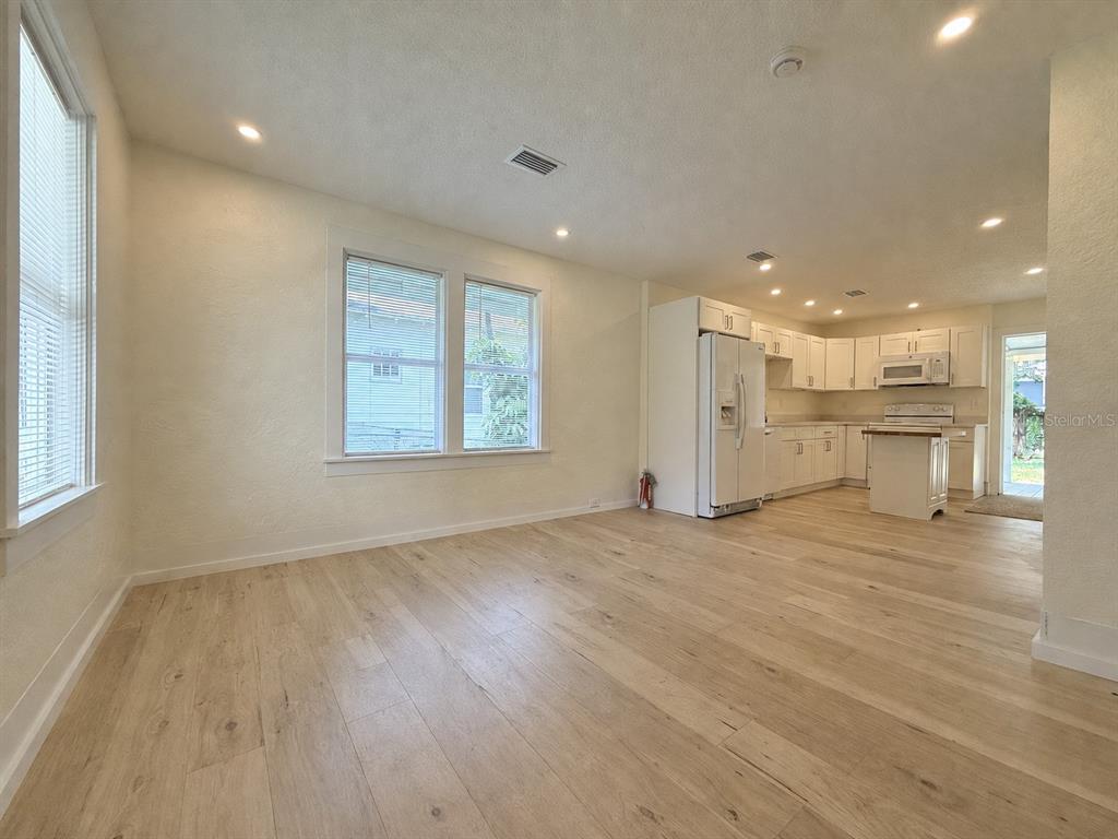 An open-concept kitchen and living area features light wood flooring and white cabinetry — 140 KINGSTON AVENUE, DAYTONA BEACH, FL