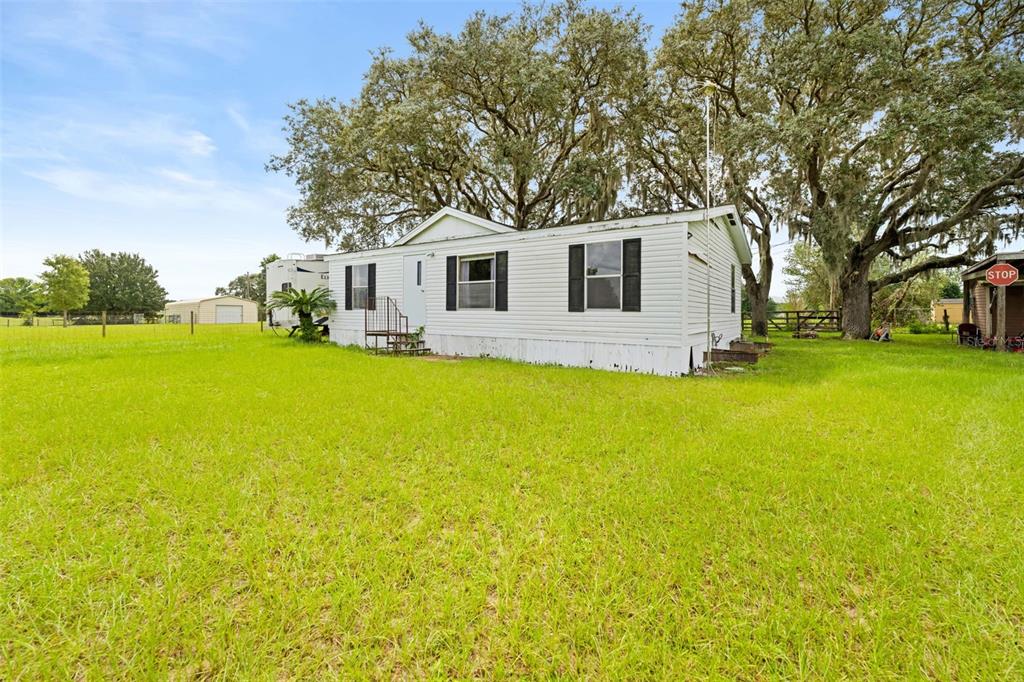 A white single-wide mobile home sits on a grassy lot under large oak trees — 4586 CALIFORNIA STREET, BROOKSVILLE, FL