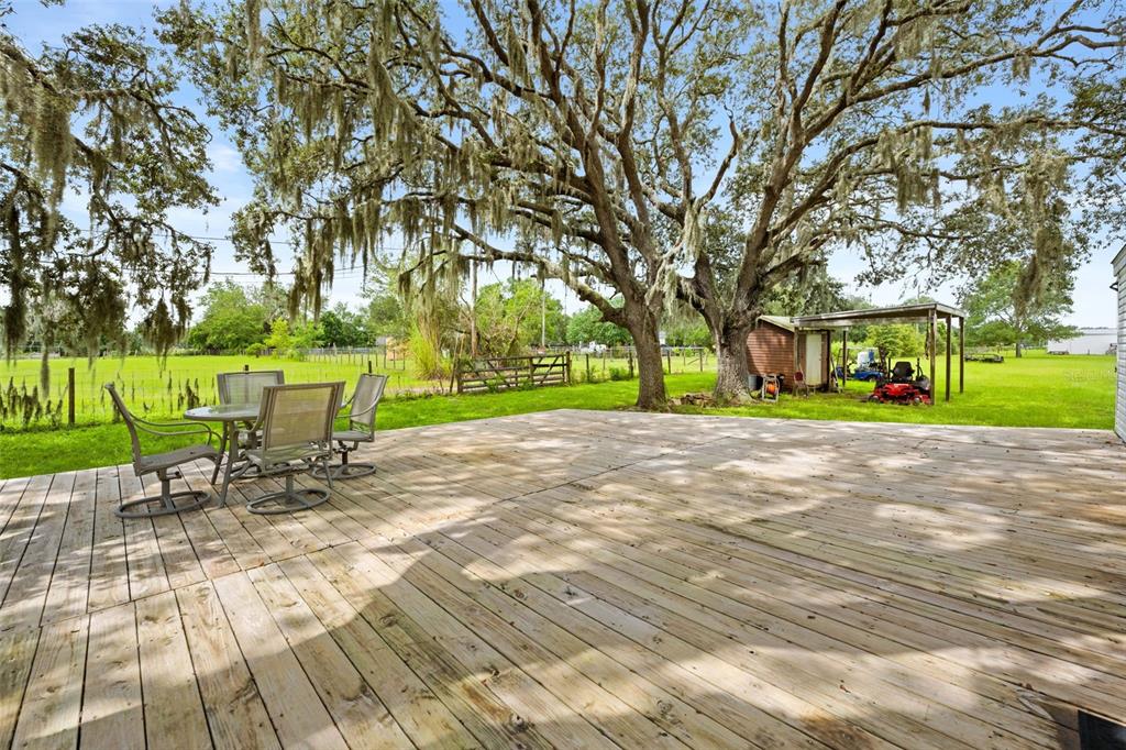 A wooden deck with patio furniture overlooks a grassy yard featuring large mossy oak trees — 4586 CALIFORNIA STREET, BROOKSVILLE, FL