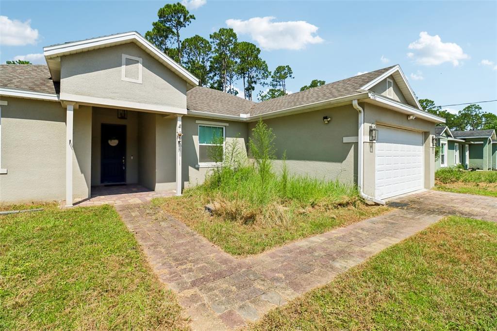 A single-story house with a beige stucco exterior, a two-car garage, and an overgrown garden — 1730 EAST PKWY, DELAND, FL