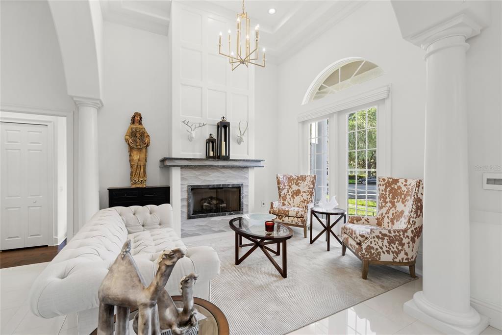 A bright living room features a fireplace, tufted sofa, cow-print chairs, and tall white columns — 11051 HAWKSHEAD COURT, WINDERMERE, FL