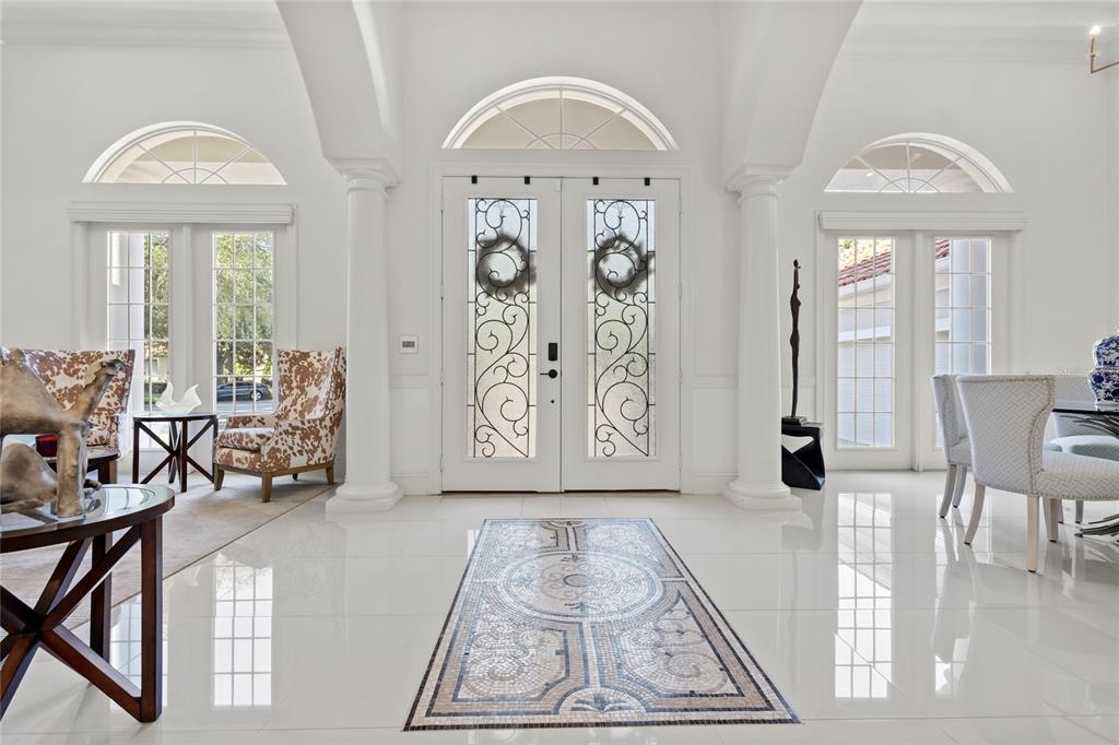 A bright foyer features white tile floors, a decorative mosaic inlay, and double glass doors — 11051 HAWKSHEAD COURT, WINDERMERE, FL