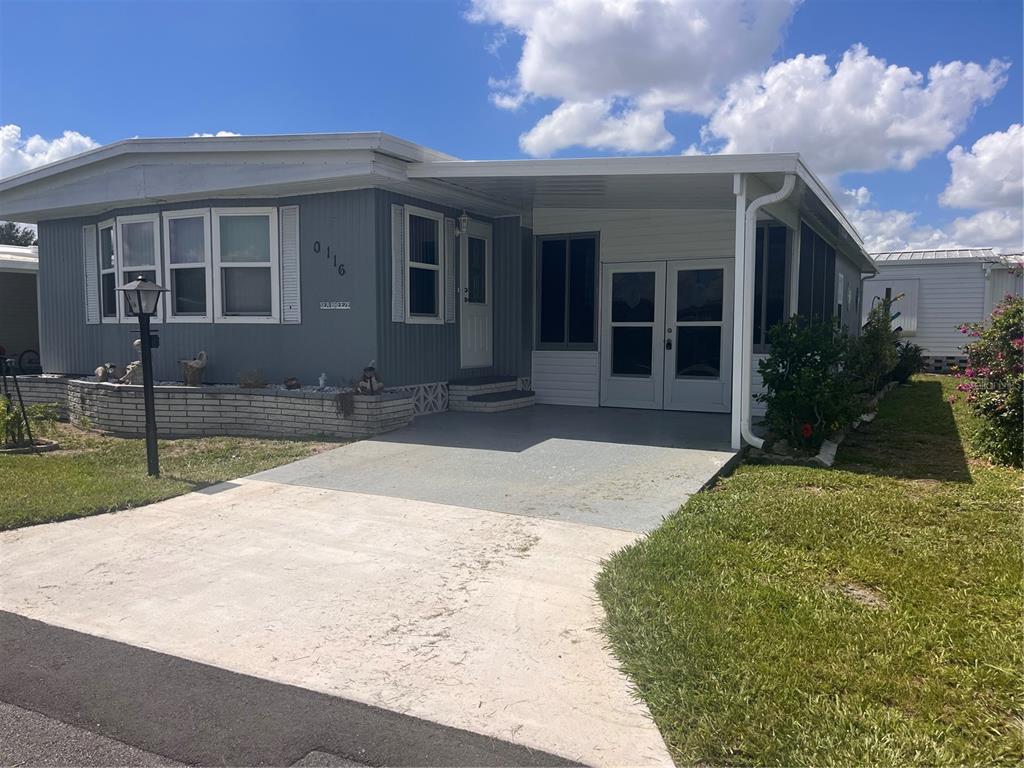 A gray manufactured home features a concrete driveway, a carport, and a brick planter box — 5316 53RD AVENUE E UNIT Q116, BRADENTON, FL