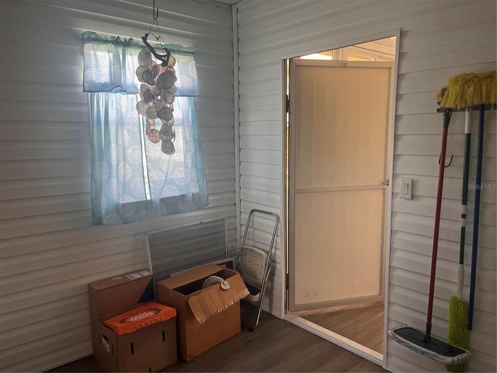 A sunroom features white horizontal siding, a window with a shell mobile, and cleaning supplies — 5316 53RD AVENUE E UNIT Q116, BRADENTON, FL
