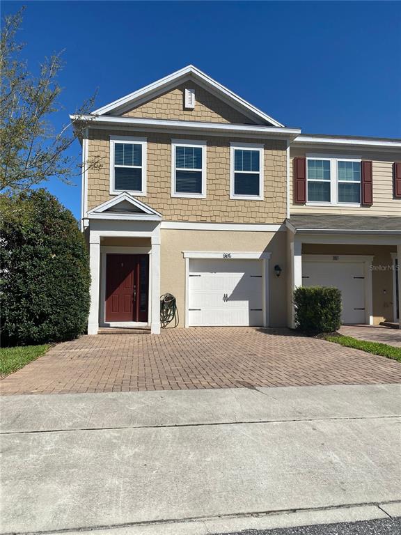 A two-story townhouse with a tan facade, red front door, and a brick paver driveway — 185 MITCHELL CREEK WAY, OVIEDO, FL