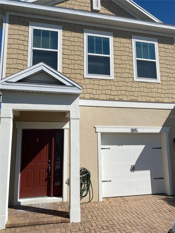 A two-story house exterior with tan shingle siding, a red front door, and a garage — 185 MITCHELL CREEK WAY, OVIEDO, FL