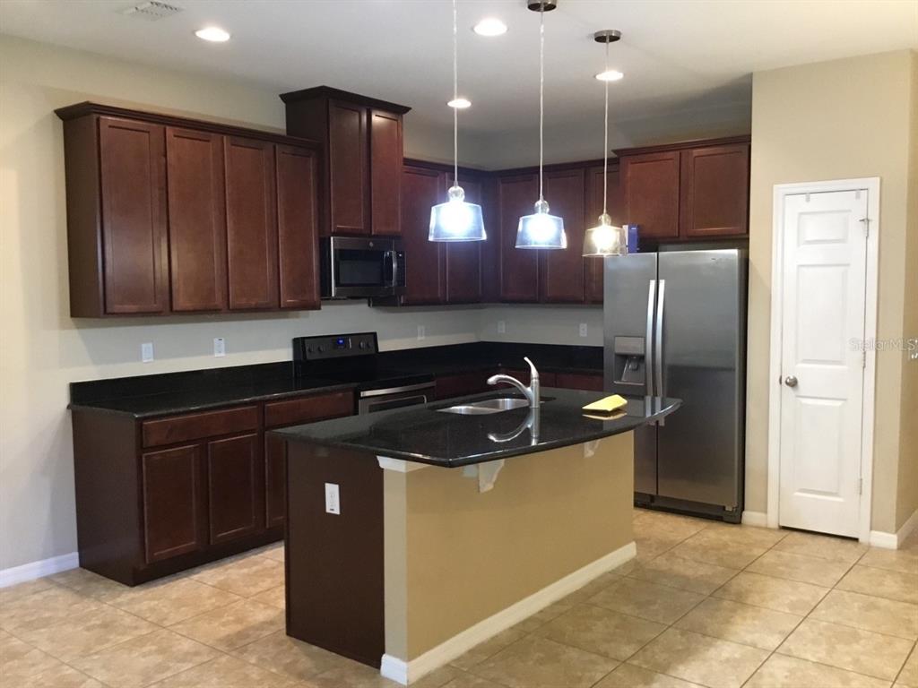 A kitchen features dark wood cabinets, black granite countertops, stainless steel appliances, and an island — 185 MITCHELL CREEK WAY, OVIEDO, FL