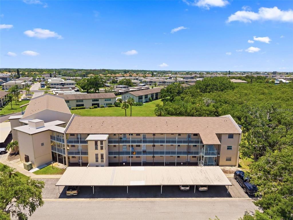 An aerial view shows a multi-story apartment building with a covered parking area in front — 5245 AMULET DRIVE UNIT 207, NEW PORT RICHEY, FL