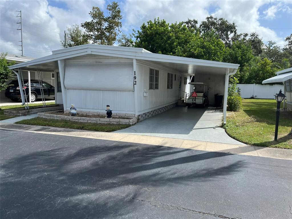 A white mobile home with a carport and a golf cart parked in the driveway — 1040 MAIN STREET UNIT 192, DUNEDIN, FL