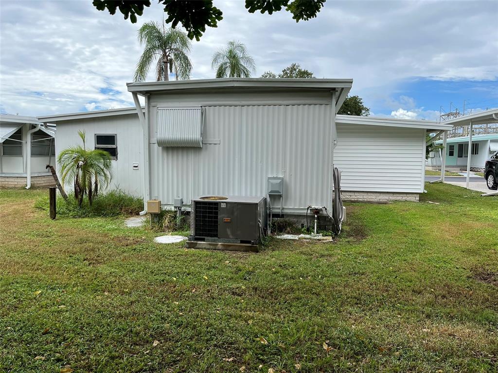 The exterior of a manufactured home features a metal-sided wall, an HVAC unit, and landscaping — 1040 MAIN STREET UNIT 192, DUNEDIN, FL