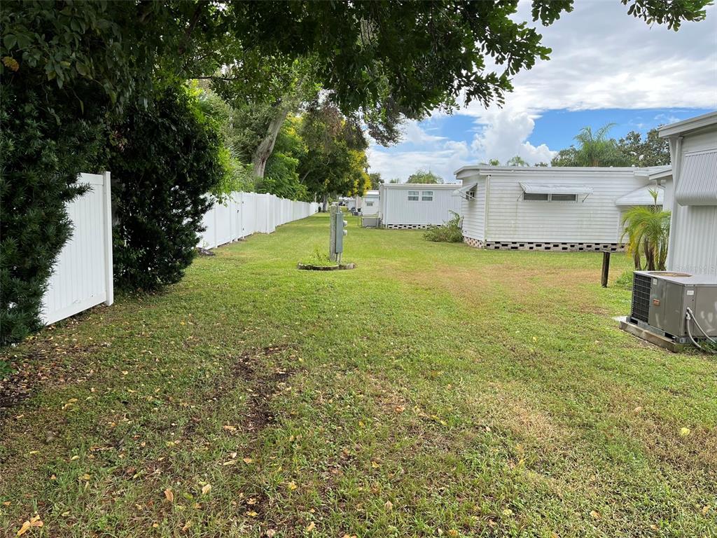 A grassy backyard area features a white vinyl fence, trees, and neighboring mobile homes — 1040 MAIN STREET UNIT 192, DUNEDIN, FL