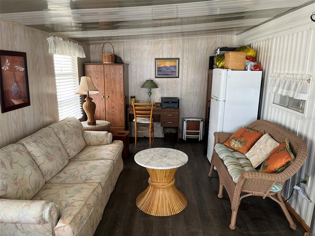 A living room features a floral sofa, a wicker loveseat, a desk, and a refrigerator — 1040 MAIN STREET UNIT 192, DUNEDIN, FL