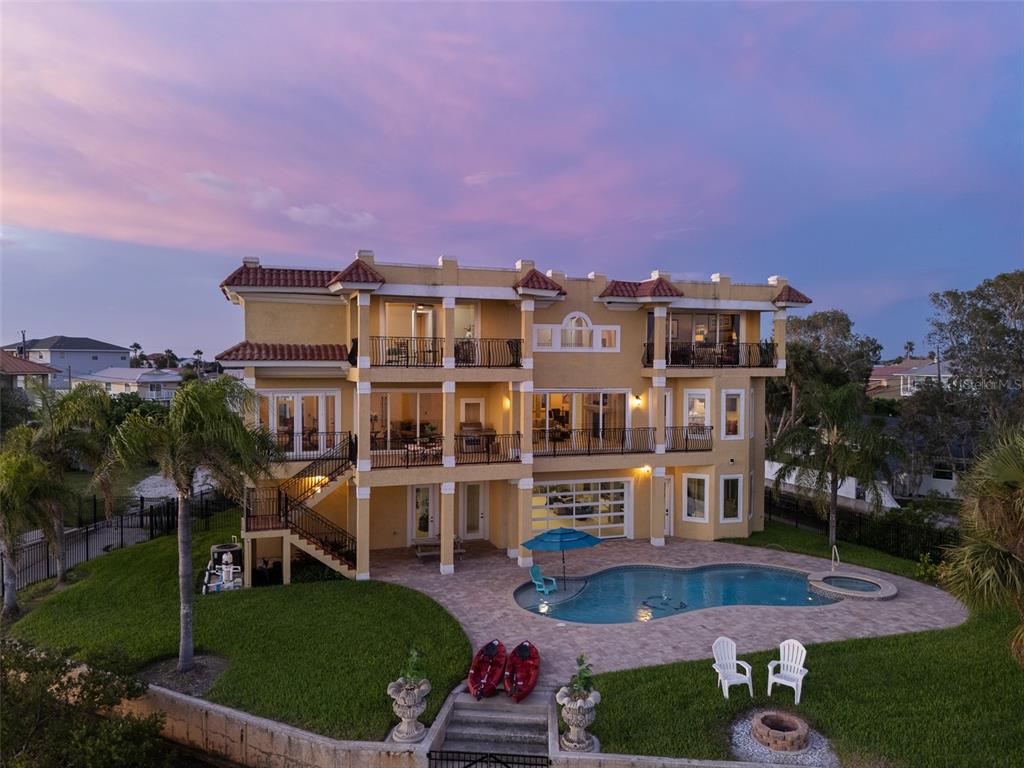 A three-story yellow house with balconies, a swimming pool, and a lawn at sunset — 3236 GULF WINDS CIRCLE, HERNANDO BEACH, FL