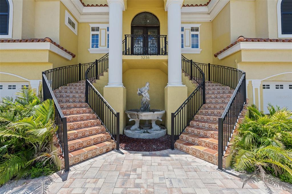 A yellow house exterior features a dual staircase leading to an elevated entrance with a fountain — 3236 GULF WINDS CIRCLE, HERNANDO BEACH, FL
