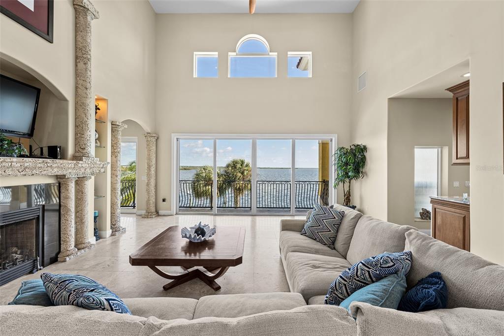 A living room with a stone fireplace, high ceilings, and large sliding doors overlooking water — 3236 GULF WINDS CIRCLE, HERNANDO BEACH, FL
