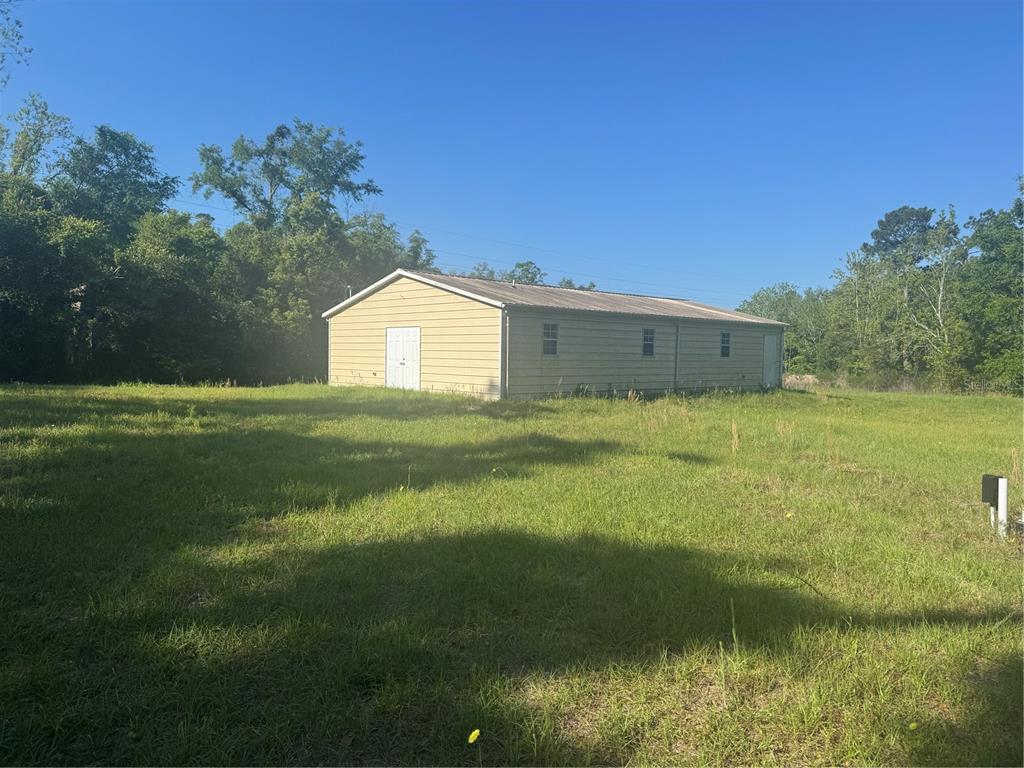 A tan metal-sided building with a gabled roof sits in a large, grassy field — 7097 119TH ROAD, LIVE OAK, FL