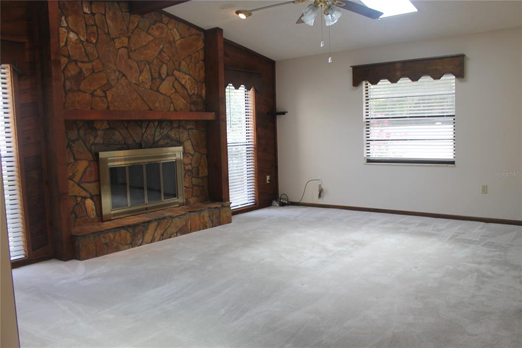 A living room features a stone fireplace, wood-paneled walls, carpeted flooring, and a ceiling fan — 8513 WINTER HAVEN DRIVE, HUDSON, FL