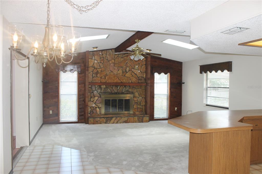A living room features a stone fireplace, wood paneling, a ceiling fan, and carpeted floors — 8513 WINTER HAVEN DRIVE, HUDSON, FL