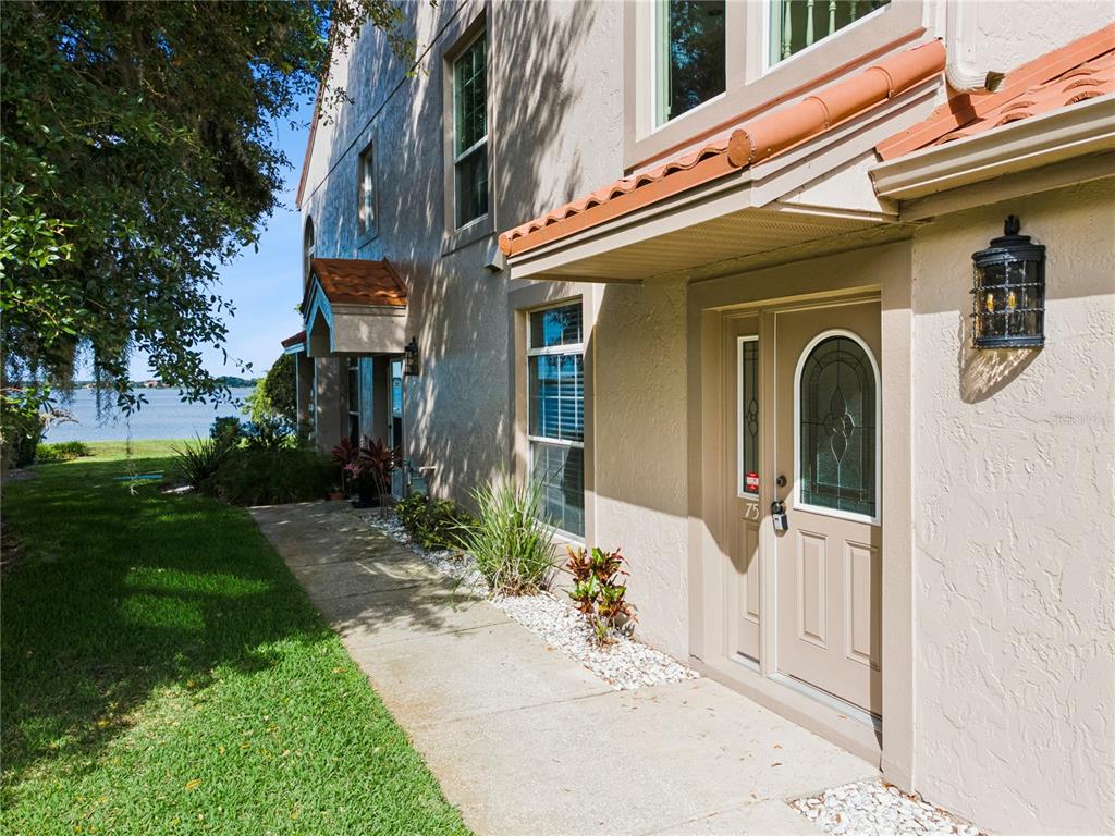 A tan stucco townhouse exterior features a front door with a decorative glass insert — 75 SUNSET VIEW DRIVE UNIT 75, WINTER HAVEN, FL