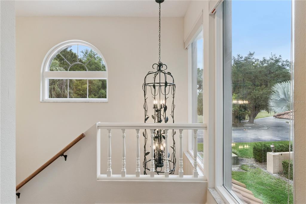 A staircase landing features a tall wrought-iron chandelier, a white railing, and a large window — 75 SUNSET VIEW DRIVE UNIT 75, WINTER HAVEN, FL