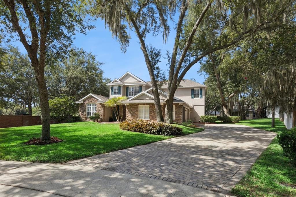 A two-story house with a stone facade, green shutters, and a paved driveway under trees — 32 CLEAR HARBOR COURT, APOPKA, FL