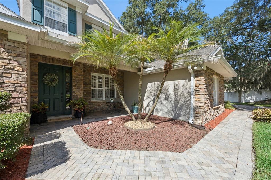 A stone-accented house exterior features a paved walkway, a palm tree, and a green door — 32 CLEAR HARBOR COURT, APOPKA, FL