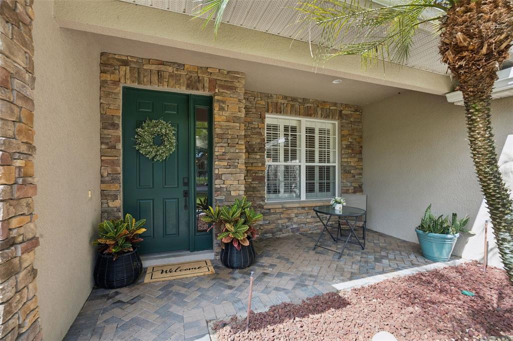 A front porch with a green door, stone facade, and a brick paver floor — 32 CLEAR HARBOR COURT, APOPKA, FL