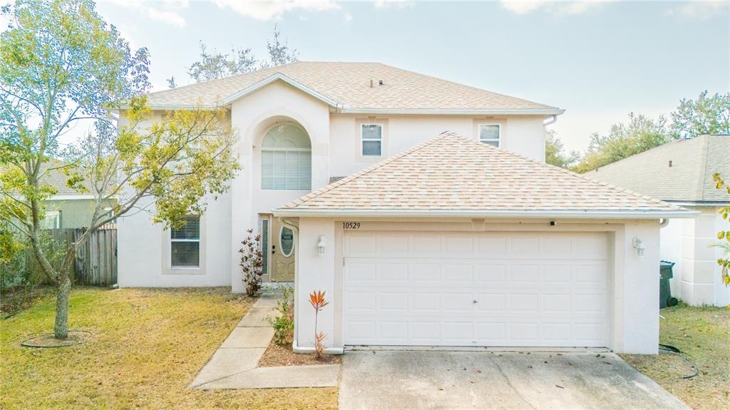 A two-story house with a beige stucco exterior, a front-facing garage, and a concrete walkway — 10529 MARONDA DRIVE, RIVERVIEW, FL