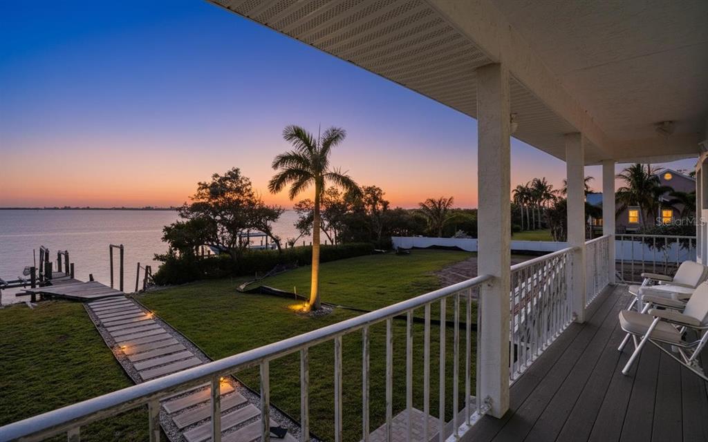 A view from a covered balcony overlooking a grassy lawn, palm tree, and the water — 10218 46TH AVENUE W, BRADENTON, FL