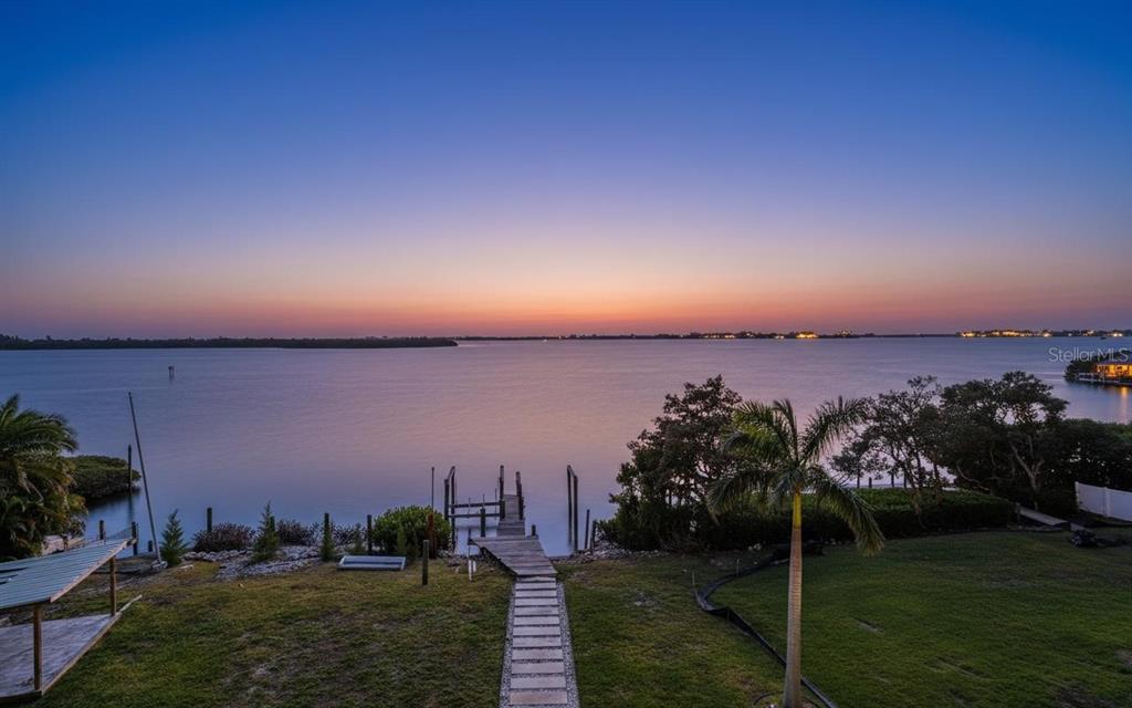 A wooden dock extends from a grassy lawn into a calm bay at sunset — 10218 46TH AVENUE W, BRADENTON, FL