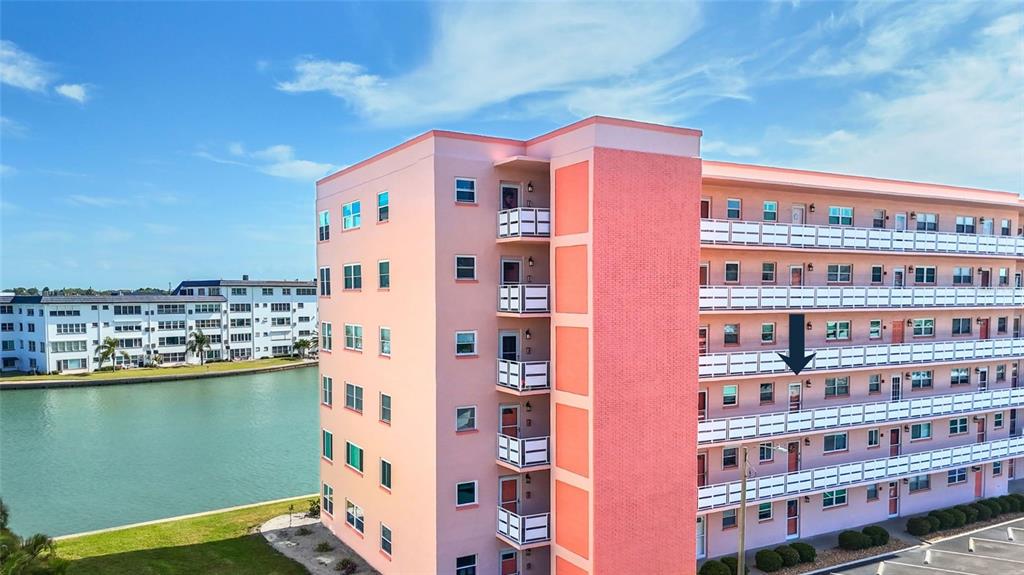 An aerial view shows a multi-story pink apartment building next to a canal — 6025 SHORE BOULEVARD S UNIT 303, GULFPORT, FL